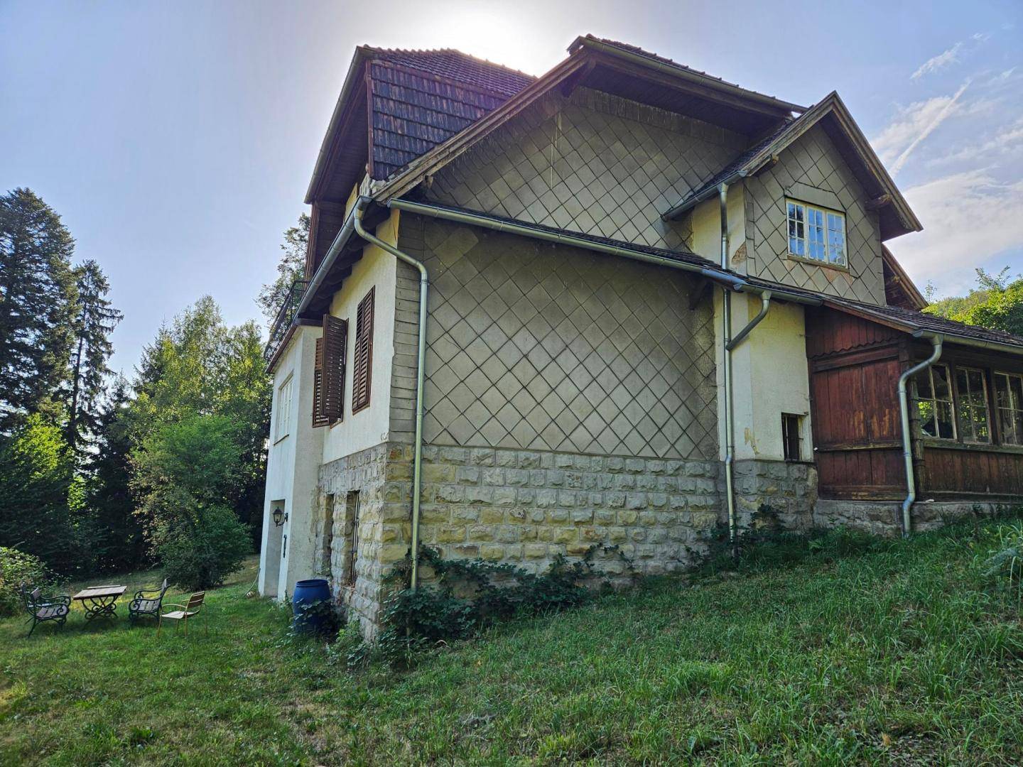 Seitenansicht des historischen Gebäudes mit Steinsockel, Schindelfassade und Gartenbereich.