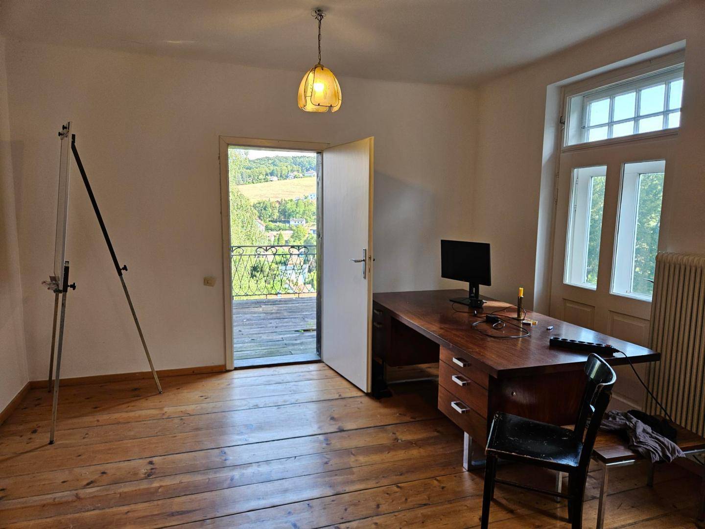 Arbeitszimmer mit Holzdielenboden, großem Schreibtisch und Zugang zu einem Balkon mit Weitblick.