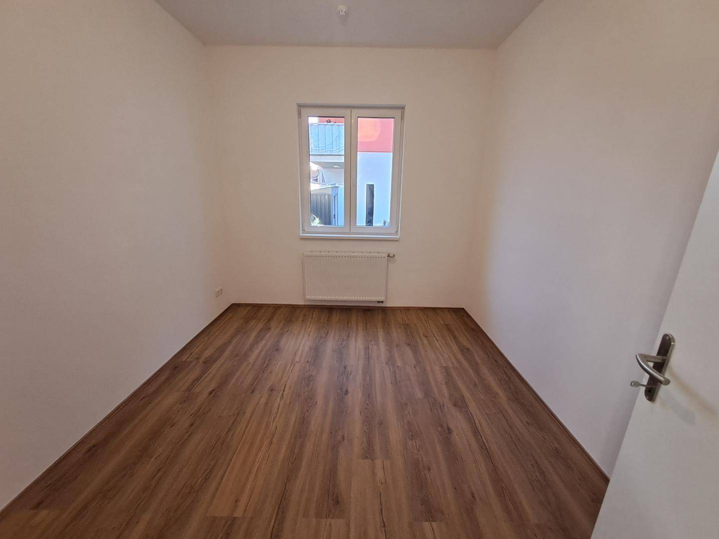 Helles Schlafzimmer mit Laminatboden und einem Fenster mit Blick ins Grüne.