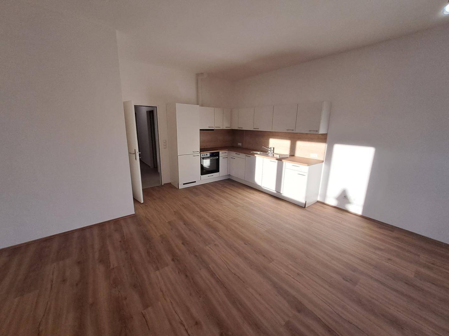 Offene Küche mit weißen Schränken, Holzarbeitsplatte und neuem Laminatboden.