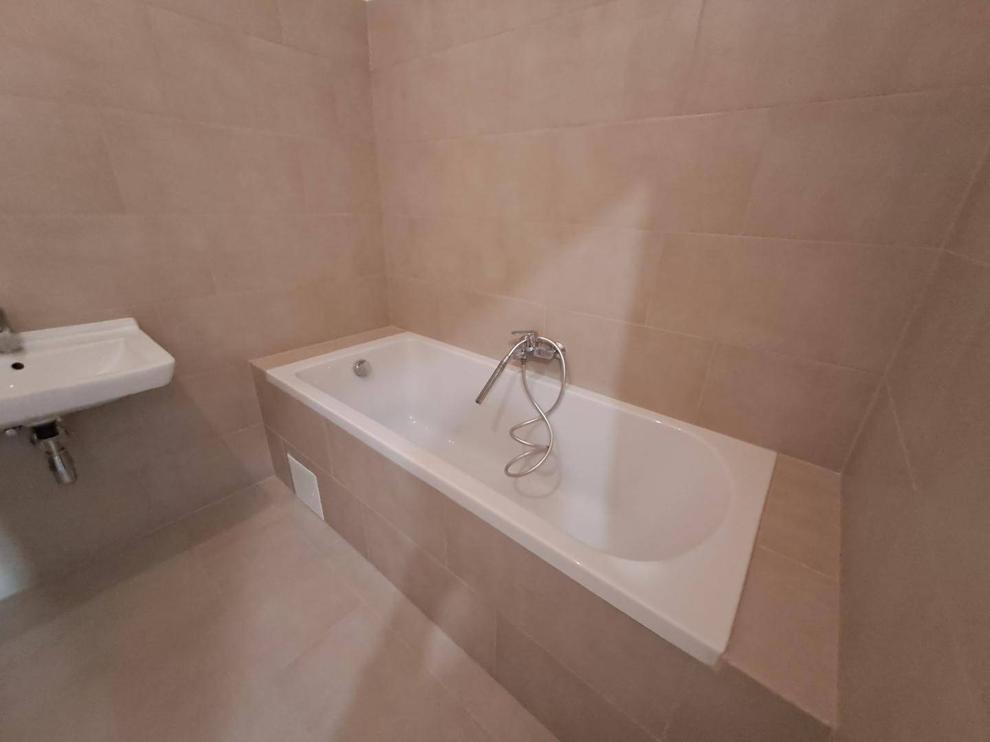 Modernes Badezimmer mit beigefarbenen Fliesen, Badewanne und kleinem Waschbecken.