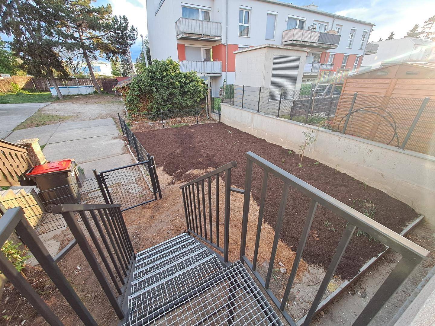 Außenbereich mit Metalltreppe, kleinem Gartenbeet und Blick auf das Mehrfamilienhaus.