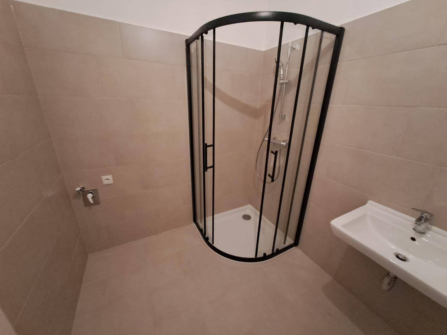 Badezimmer mit beigefarbenen Fliesen, Duschkabine und Waschbecken.
