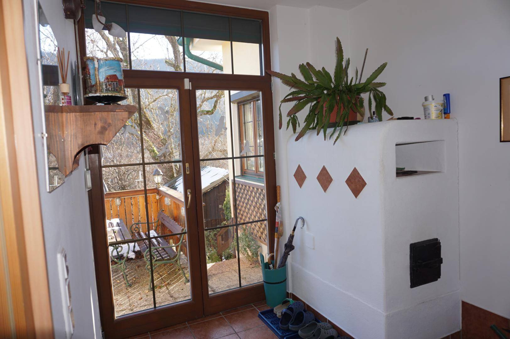 Eingangsbereich mit Kachelofen und Terrassenzugang durch große Glastüren.