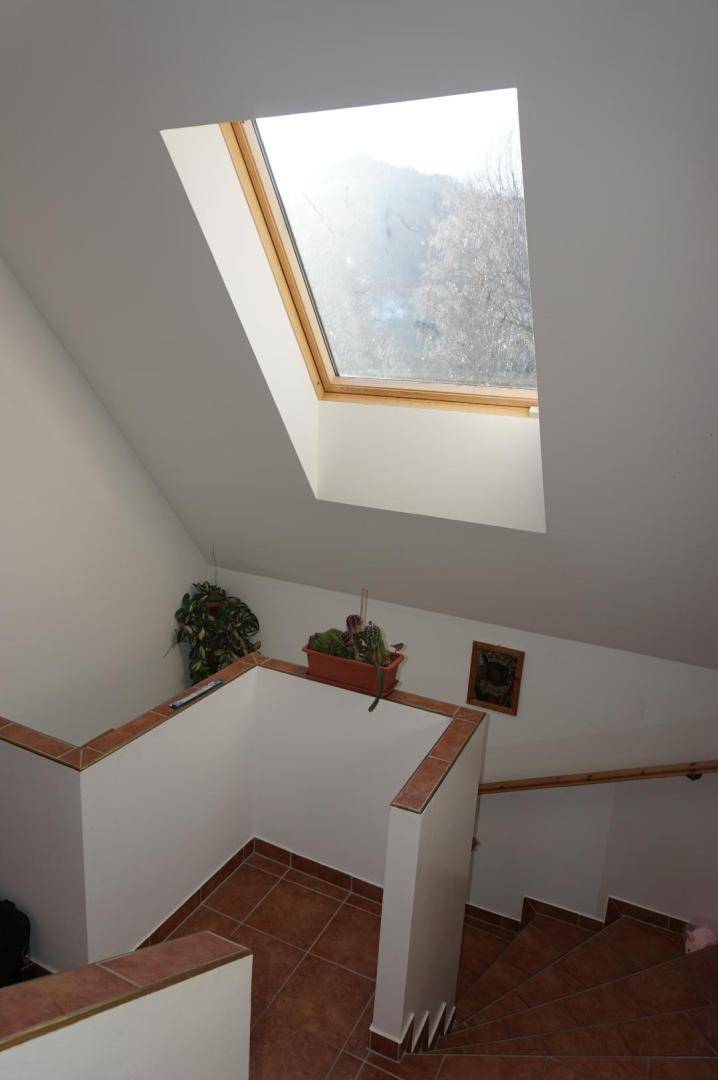 Treppenhaus mit Terrakottafliesen und einem großen Dachfenster, das viel Licht spendet.