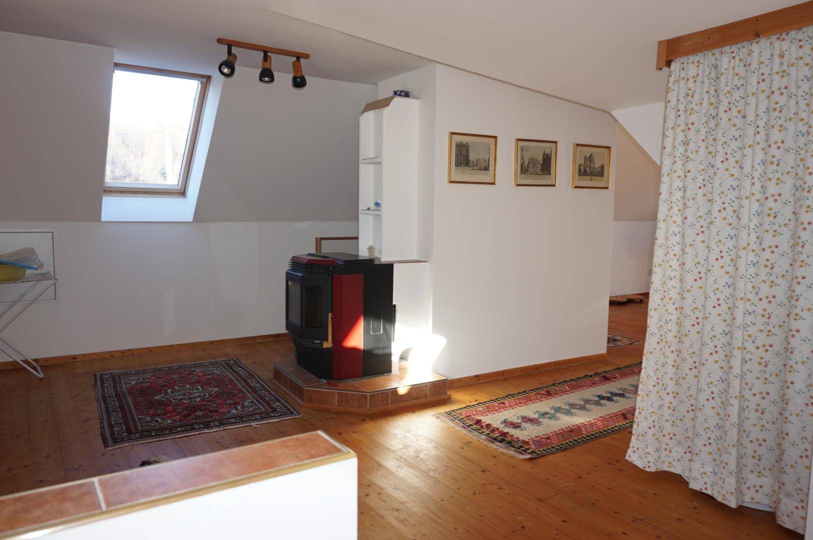 Dachgeschossraum mit Holzboden, Kaminofen und Dachfenster für natürliches Licht.