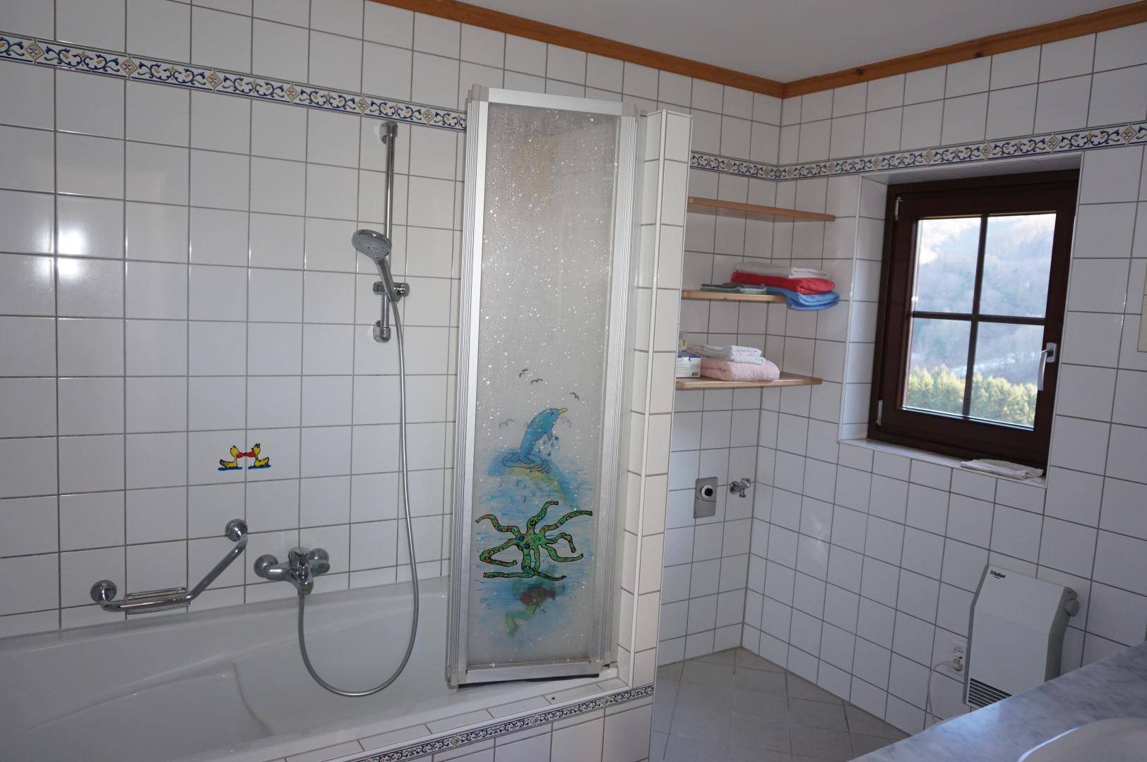 Badezimmer mit weißen Fliesen, Badewanne mit Duschabtrennung und Fenster.