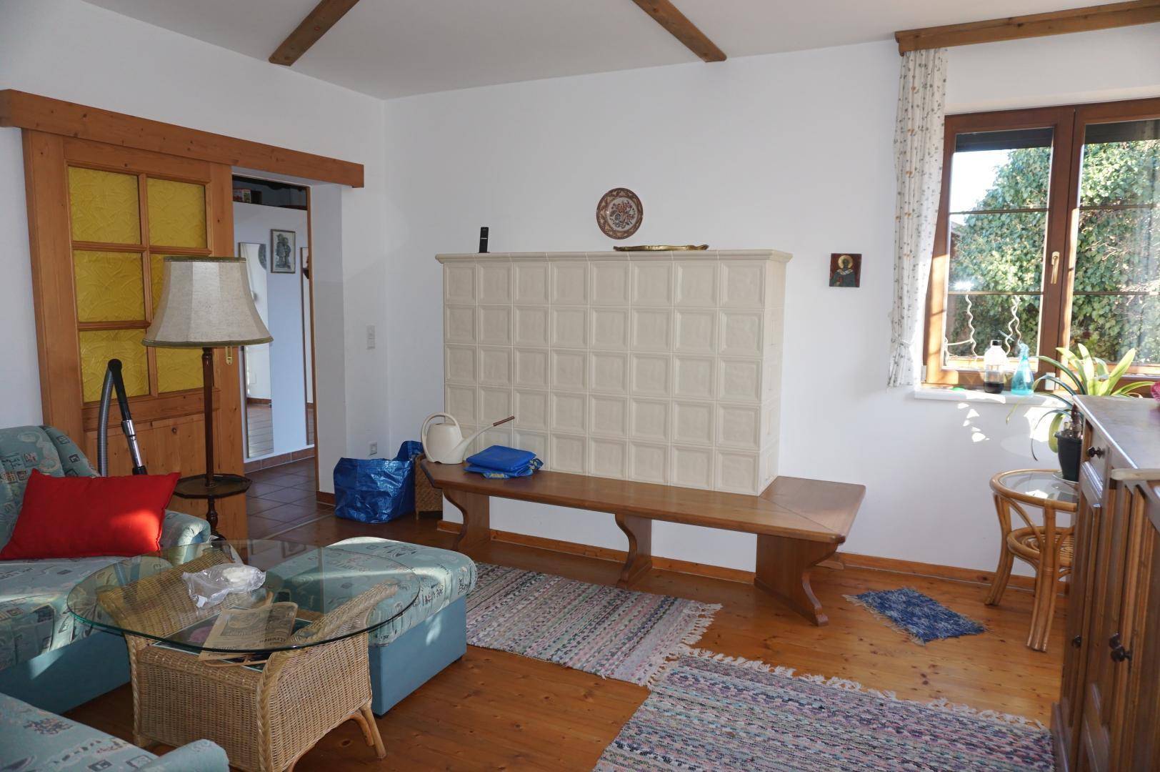 Gemütliches Wohnzimmer mit Holzboden, Kachelofen und Blick ins Grüne.