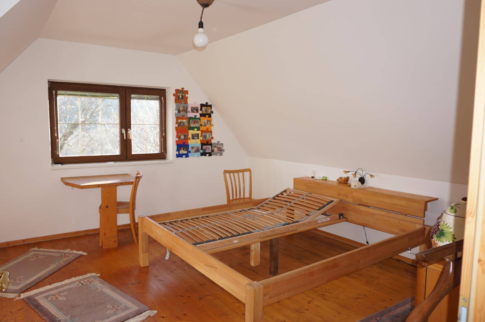 Schlafzimmer mit Holzboden, Dachschräge und einem Fenster mit Blick ins Grüne.