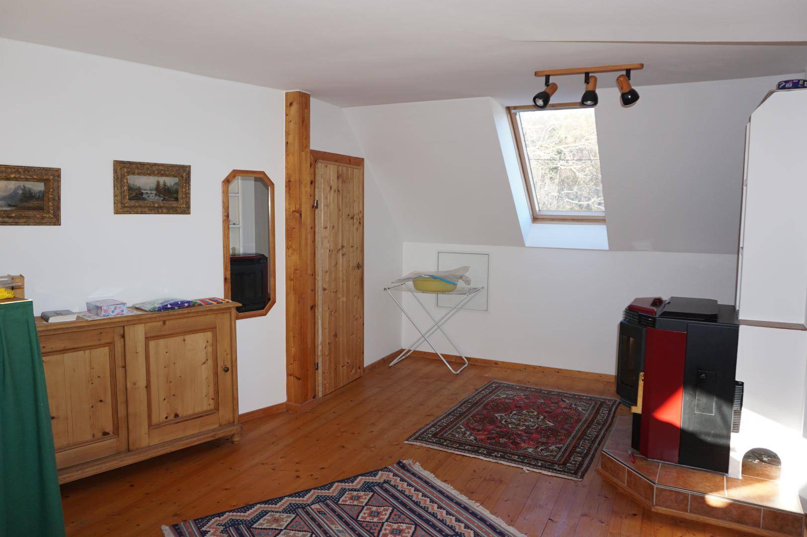 Gemütlicher Dachgeschossraum mit Holzboden, Kaminofen und rustikalen Holzmöbeln.