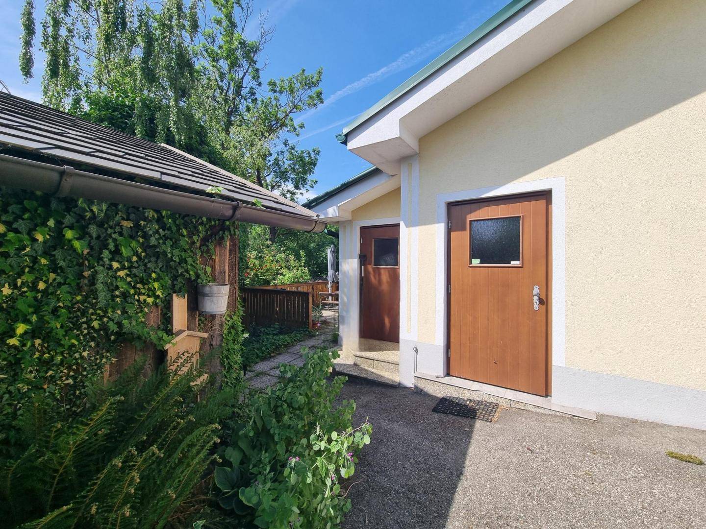 Eingangsbereich des Hauses mit zwei Holztüren und einer überdachten Seitenpartie.