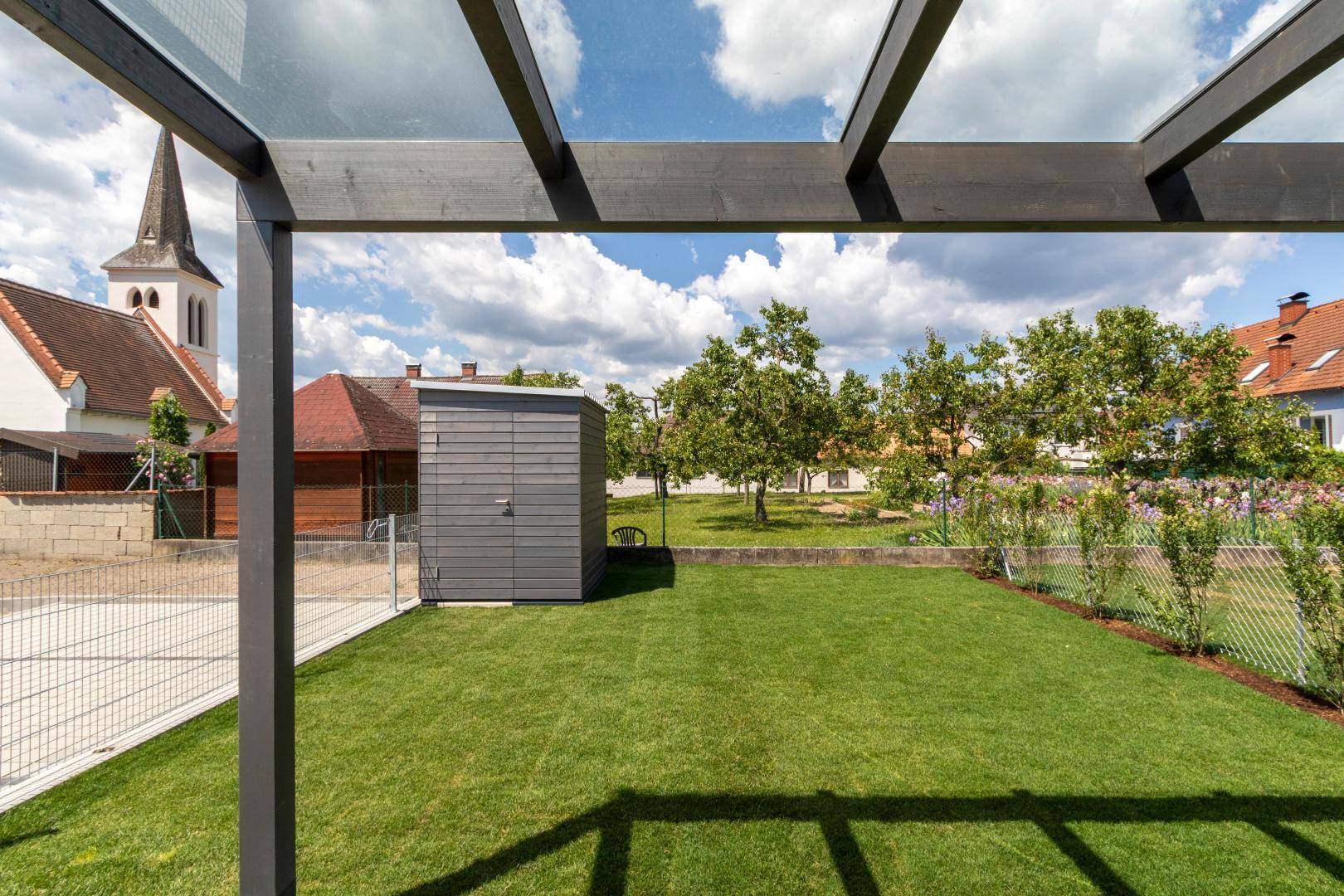 Grüner Gartenbereich mit Rasenfläche, Gartenhaus und Blick auf die Kirche im Hintergrund.