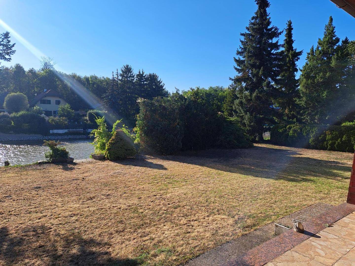 Großer Gartenbereich mit Rasenfläche und Blick auf den See, umgeben von Bäumen.