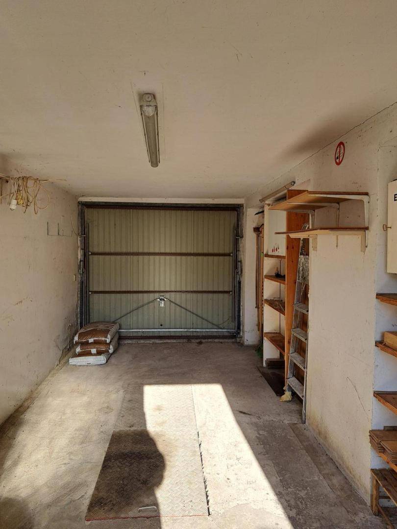 Geräumige Garage mit Rolltor, Betonboden und Regalen für Lagerzwecke.