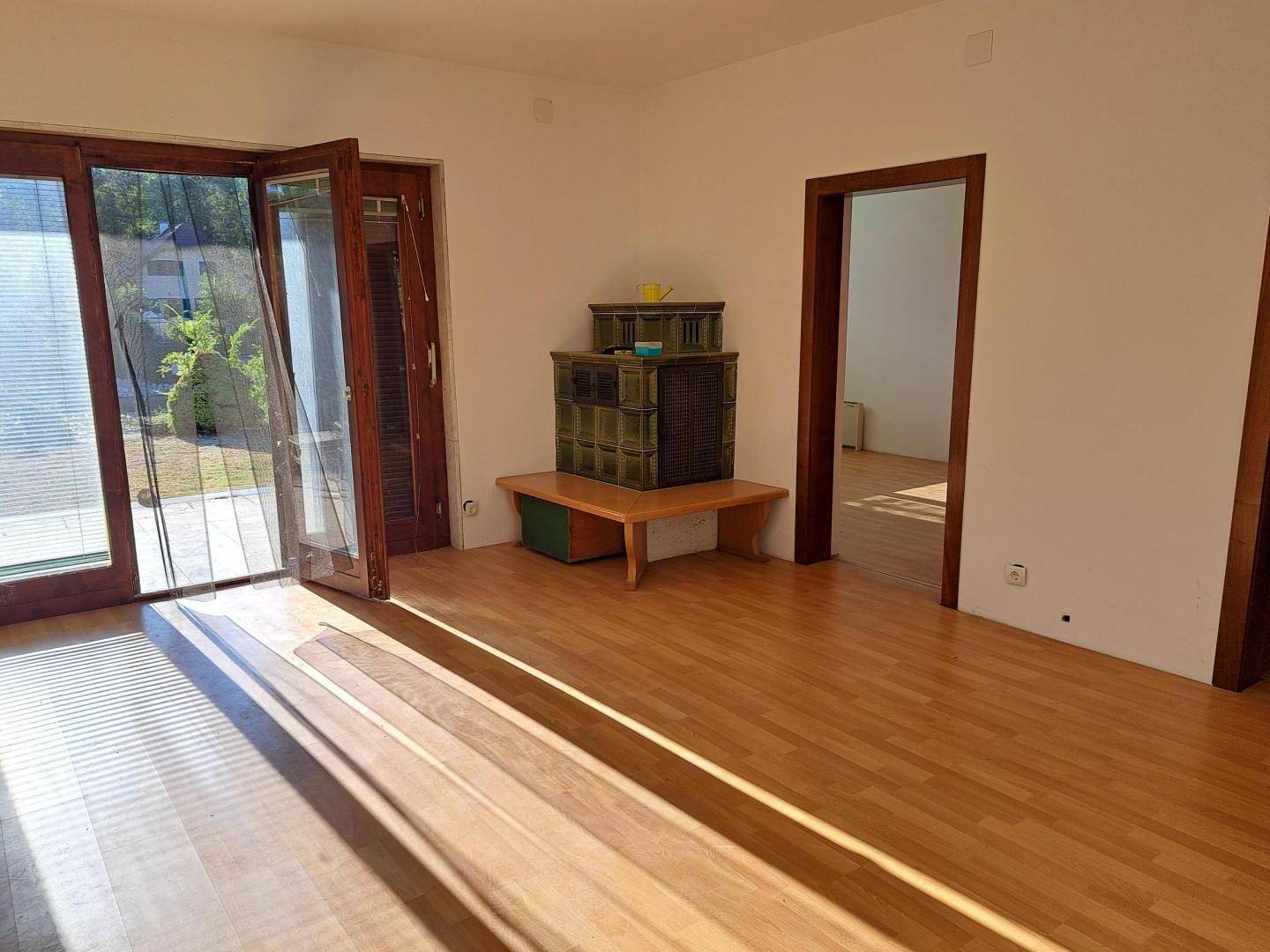 Helles Wohnzimmer mit Holzboden, großen Glastüren und einem traditionellen Kachelofen.