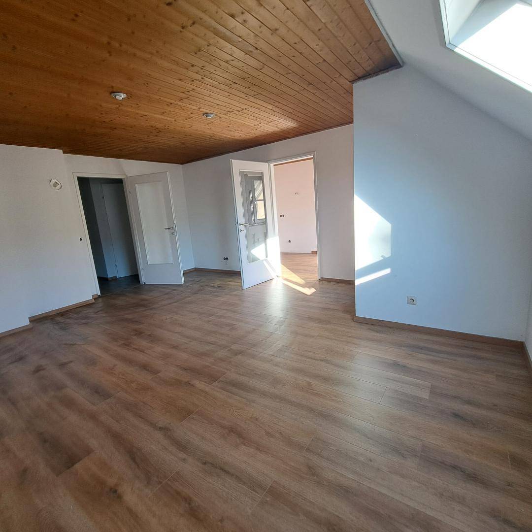 Heller Wohnbereich mit Holzlaminatboden, Holzdecke und Dachfenster, das viel Tageslicht hereinlässt.