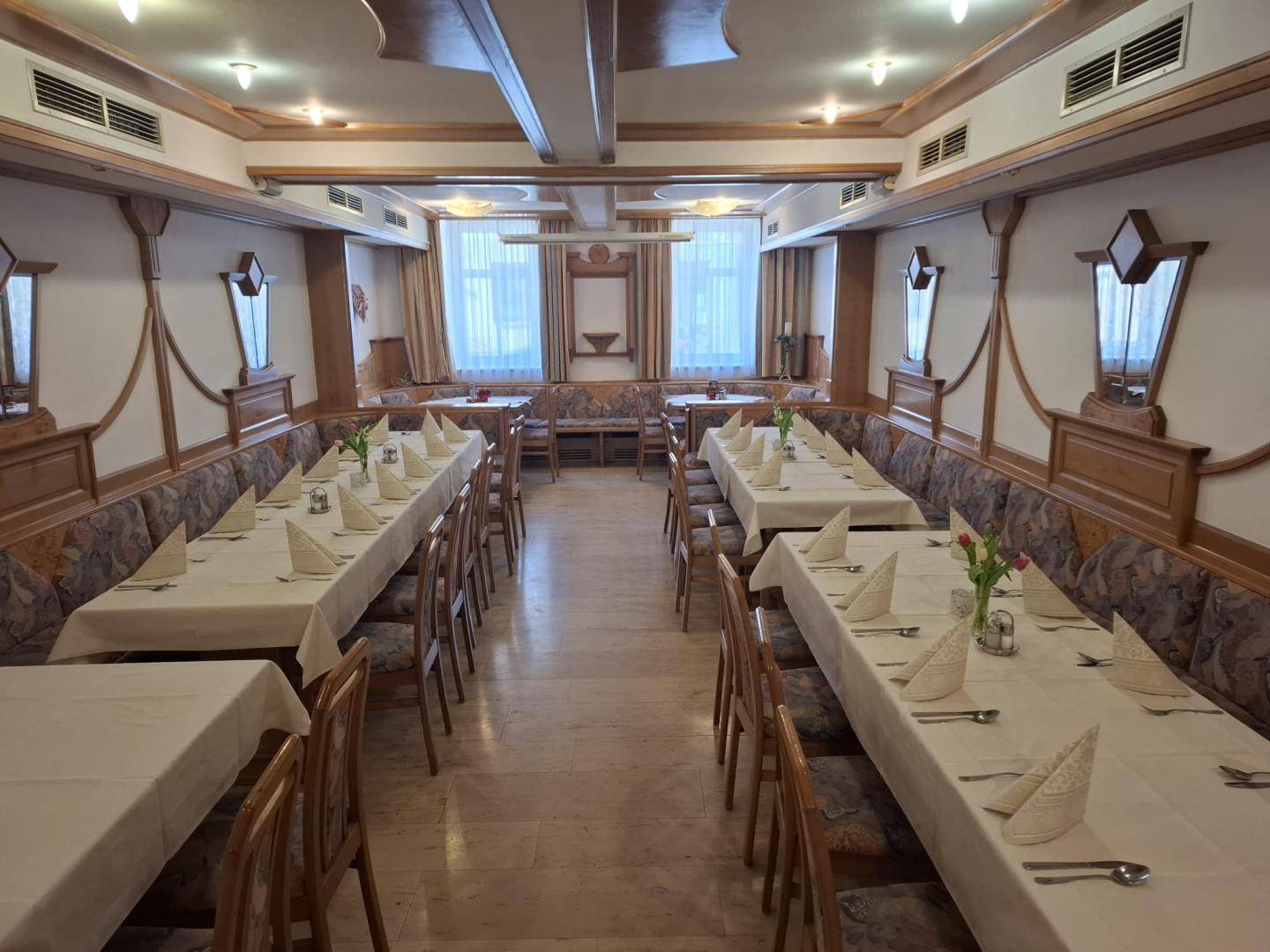 Langer Speisesaal mit traditioneller Holzvertäfelung, gepolsterten Bänken und gedeckten Tischen.