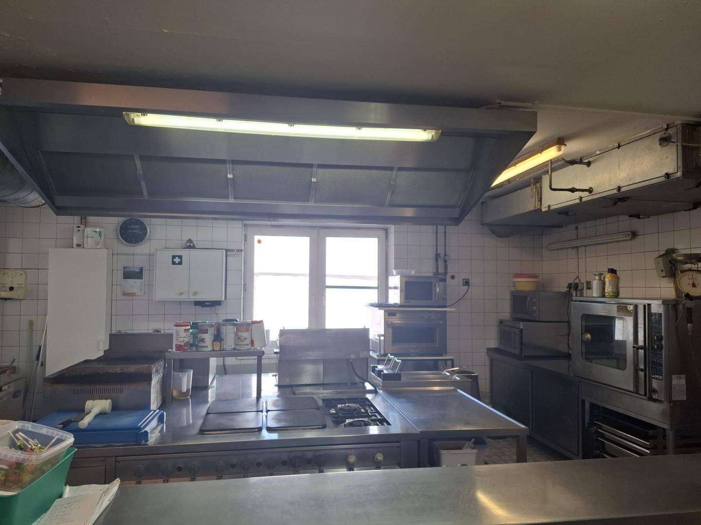 Professionelle Großküche mit Edelstahlgeräten, Ablufthaube und einem Fenster.