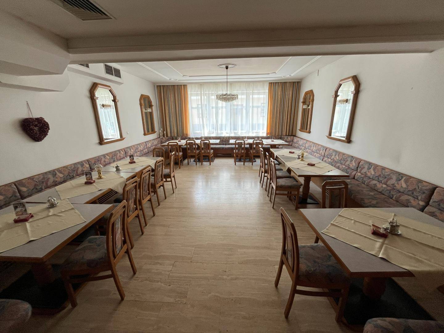 Heller Speisesaal mit großen Fenstern, gepolsterten Bänken und vielen Tischen für Veranstaltungen.