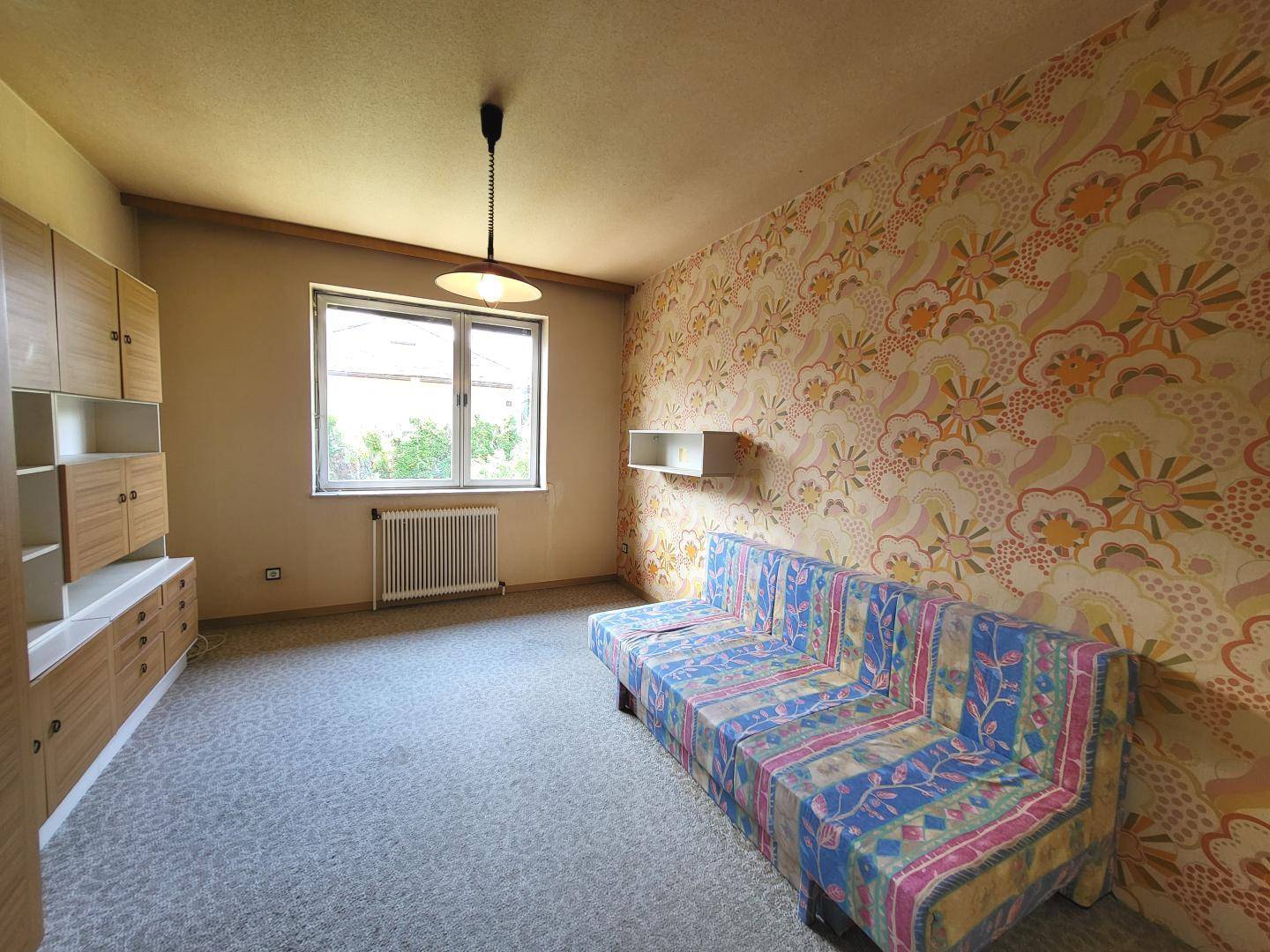 Zimmer mit auffälliger Tapete, Teppichboden und einem Schlafsofa.