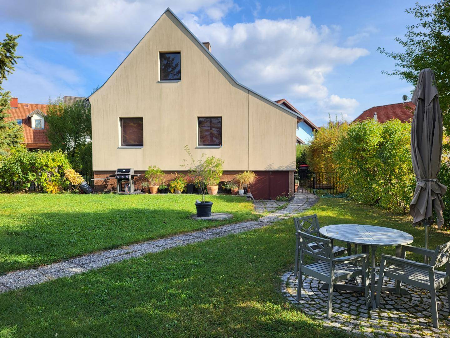 Rückansicht des Hauses mit großem Rasen, Sitzgelegenheiten und Sonnenschirm im Garten.