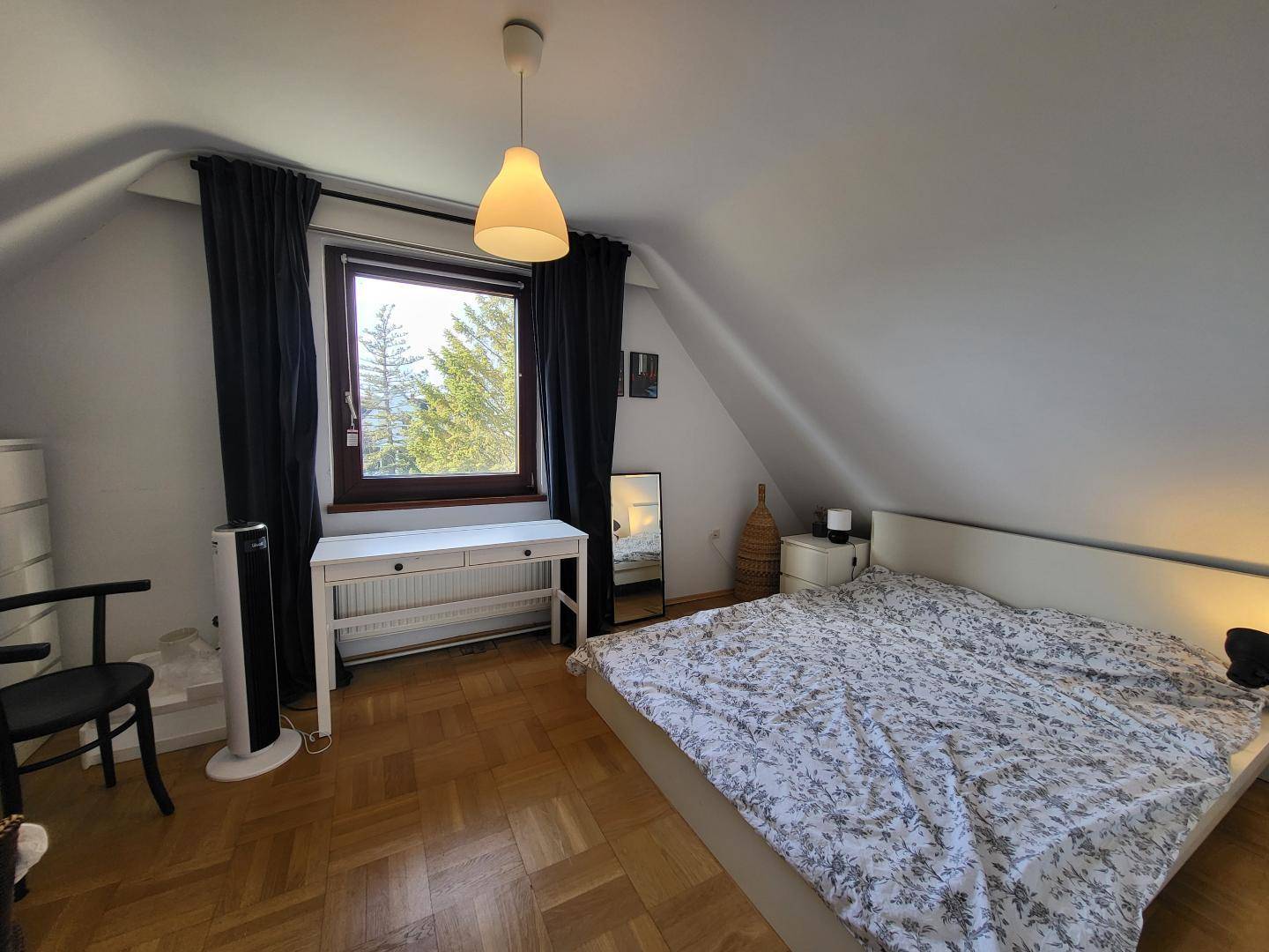 Helles Schlafzimmer im Dachgeschoss mit Holzboden, großem Bett und Fenster.