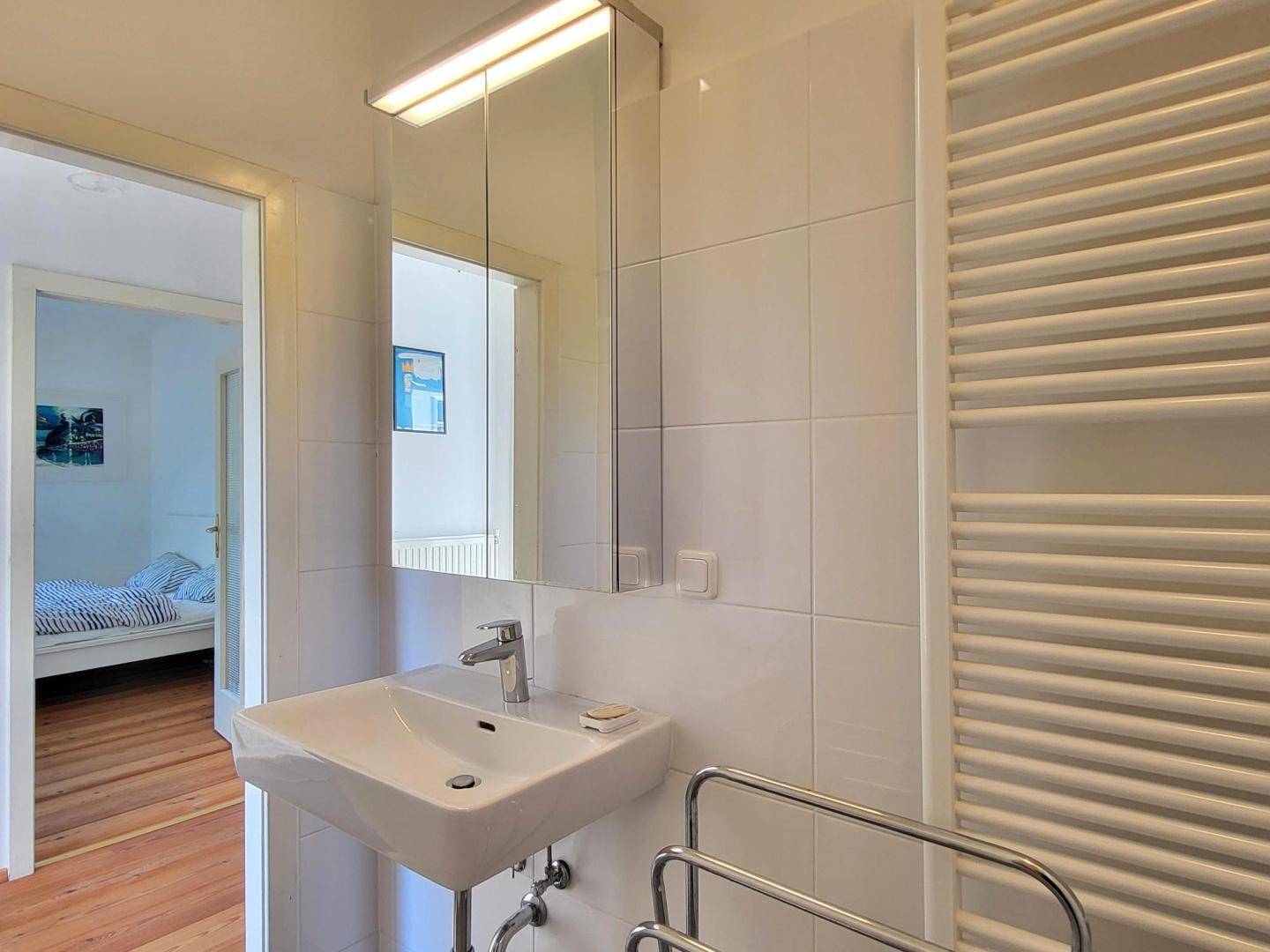 Helles Badezimmer mit Waschbecken, Spiegelschrank und beheiztem Handtuchhalter.