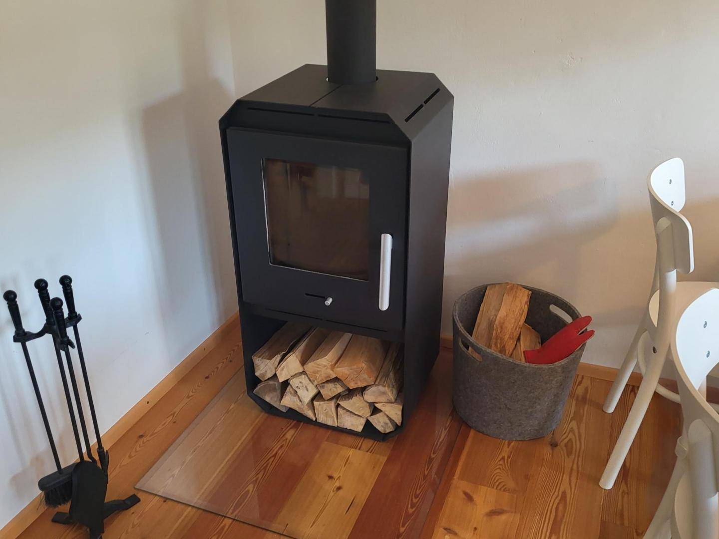 Moderner Holzofen mit Brennholz und Kaminbesteck auf Holzboden.