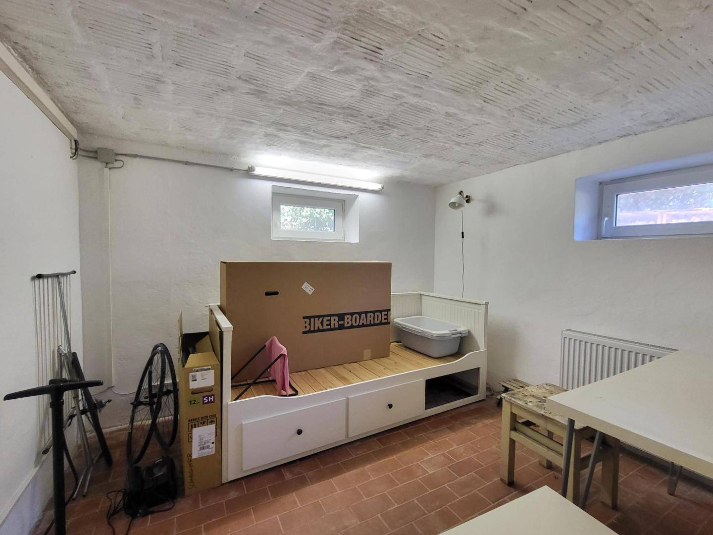 Geräumiger Kellerraum mit Fliesenboden, Tagesbett und kleinem Fenster.