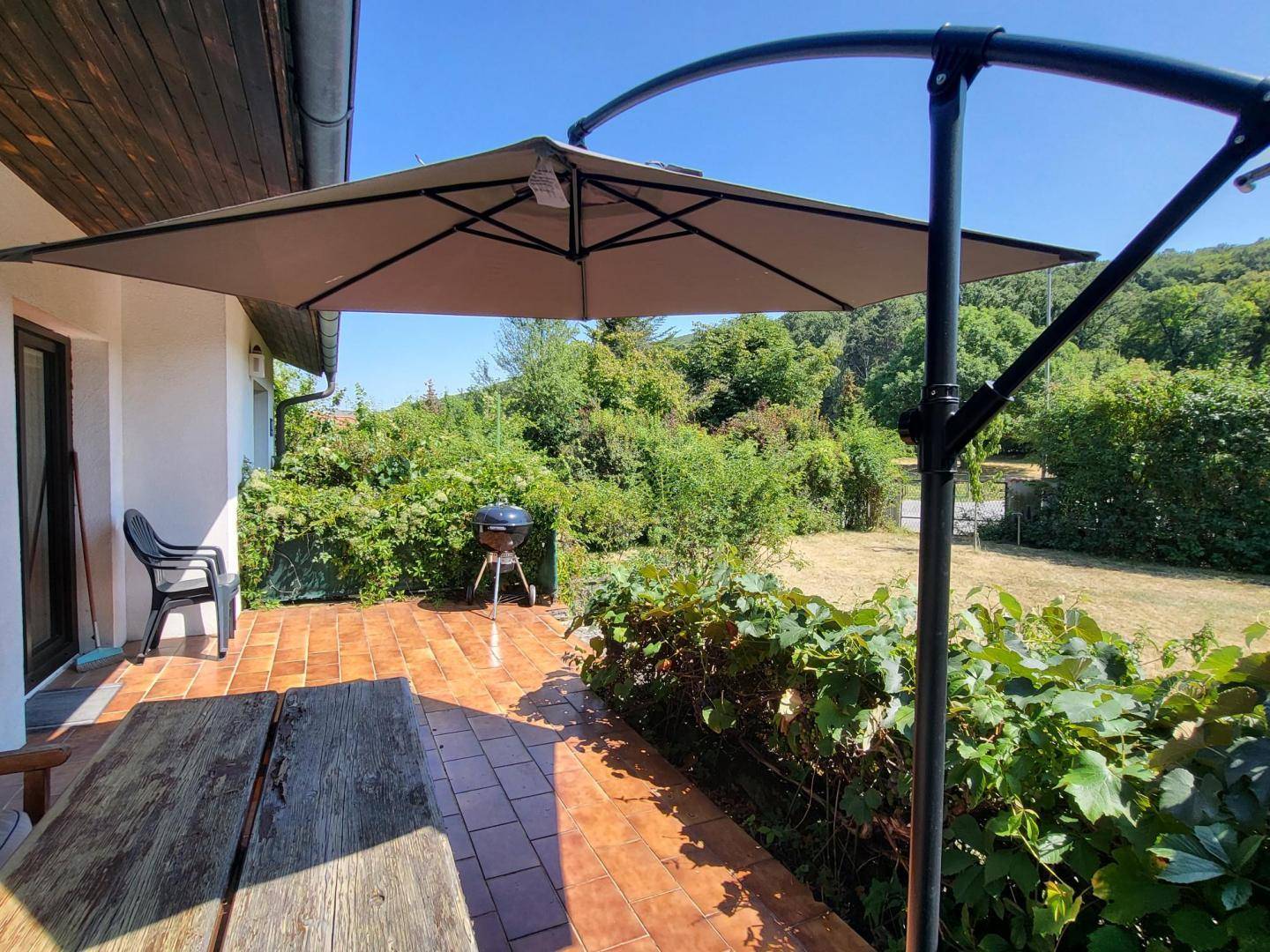 Sonniger Terrassenbereich mit Grill, Holztisch und Blick ins Grüne.