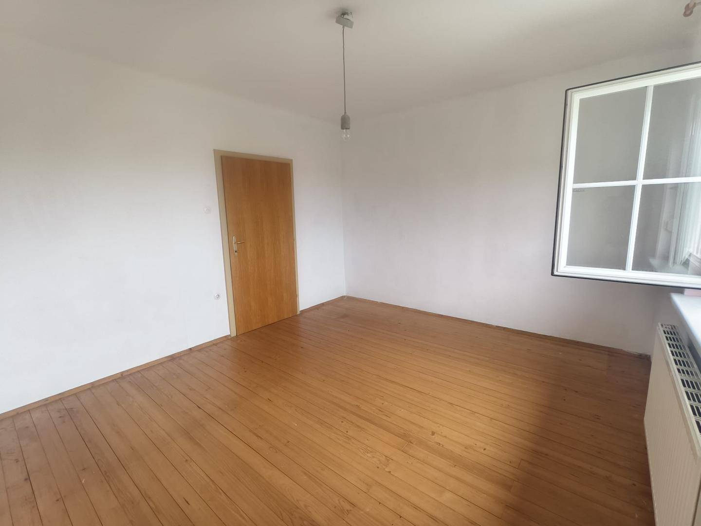 Helles Zimmer mit Holzdielenboden und einer Holztür, bereit zur individuellen Gestaltung.