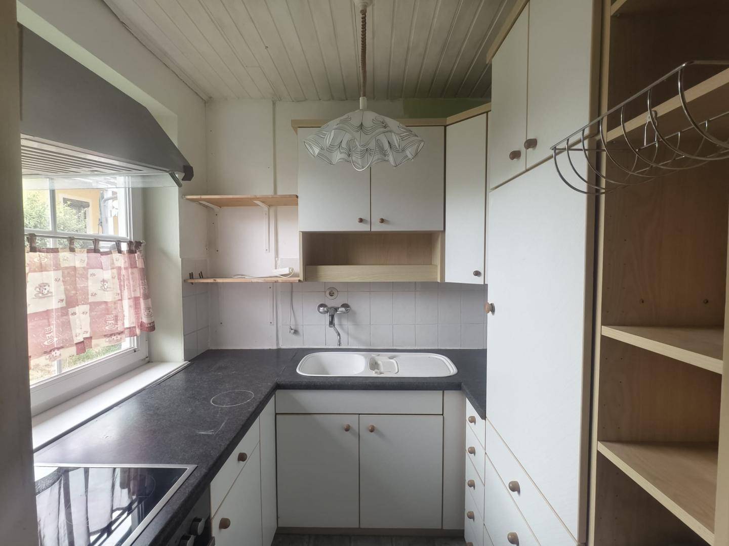 Helle Küche mit weißen Schränken, dunkler Arbeitsplatte, Spüle und Kochfeld, mit Fenster.