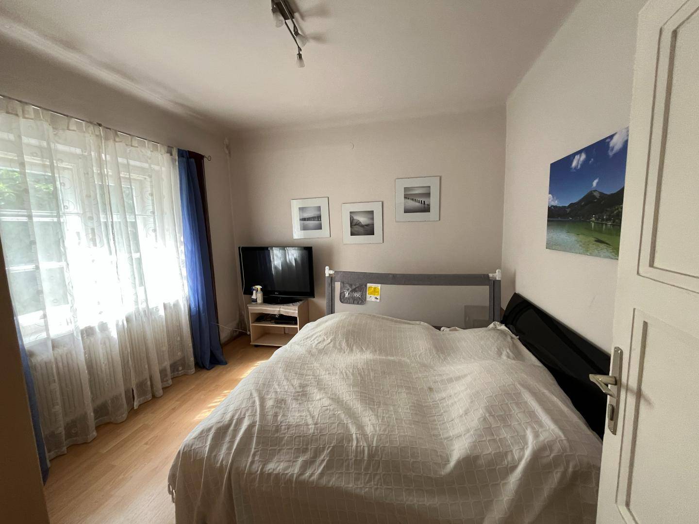 Helles Schlafzimmer mit Doppelbett, Fenster und einfacher Einrichtung.