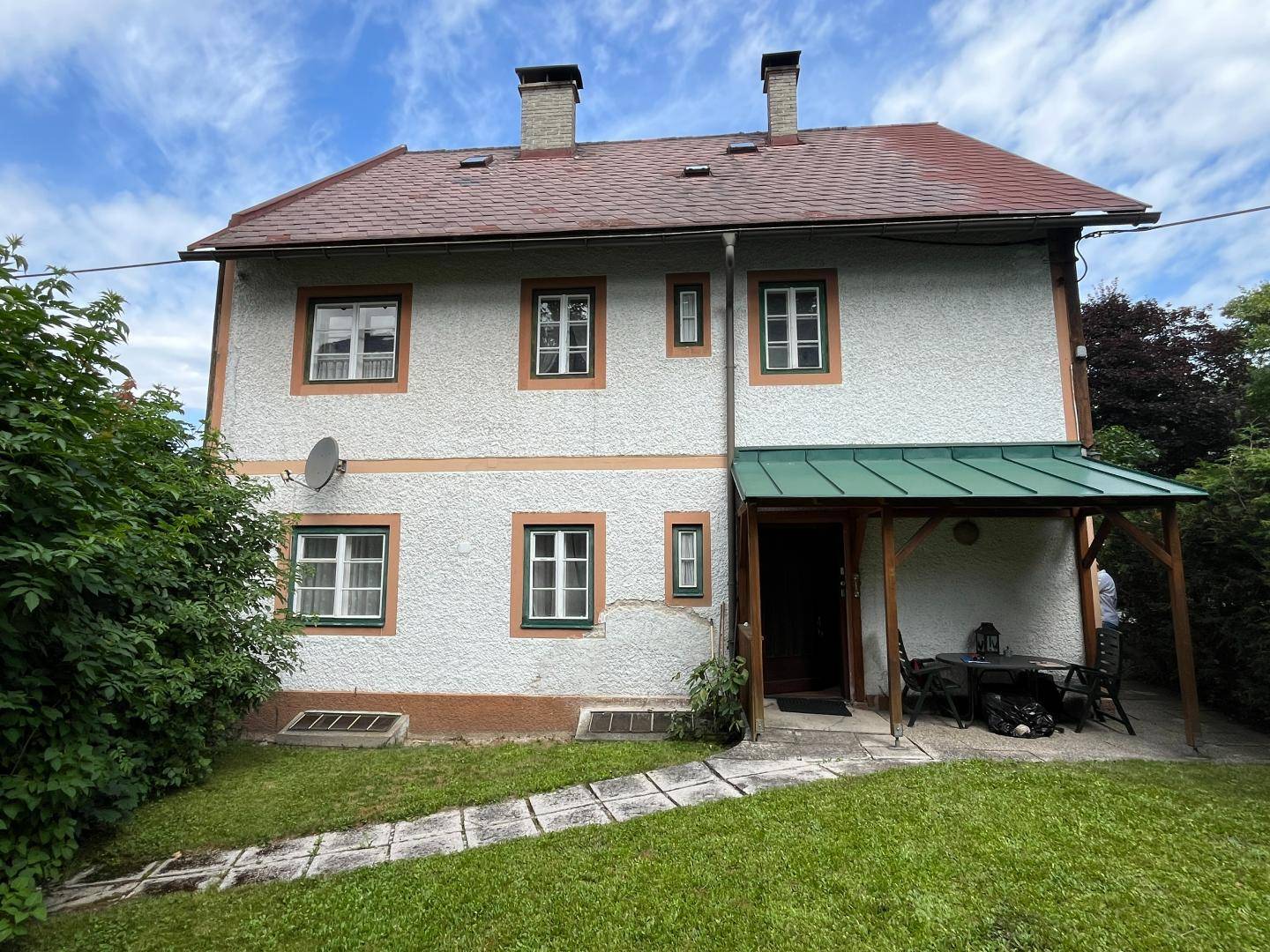 Rückseite des Hauses mit grünem Garten, Rasenfläche und überdachtem Sitzbereich.