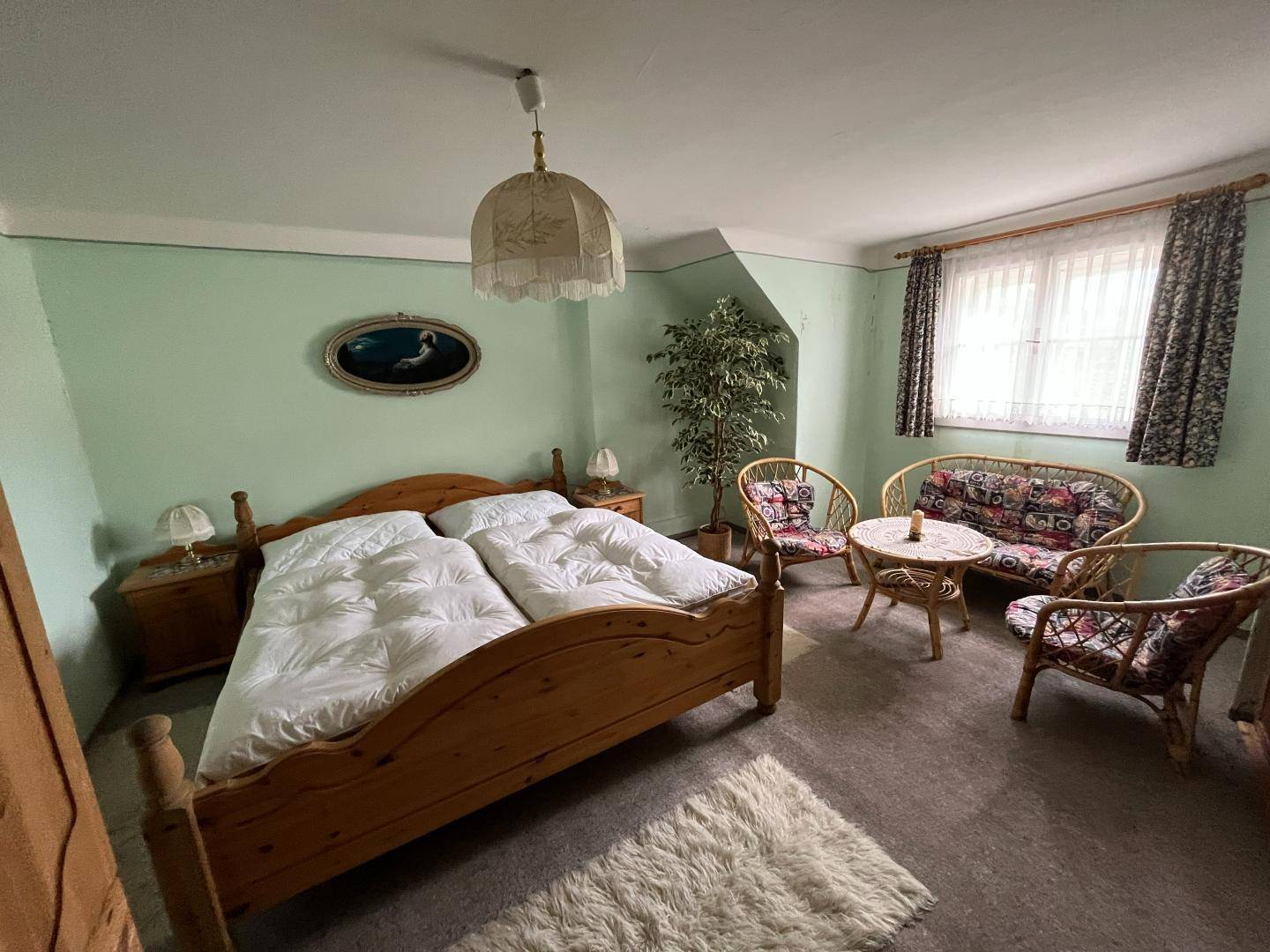 Schlafzimmer mit Doppelbett, Rattanmöbeln und hellgrünen Wänden.