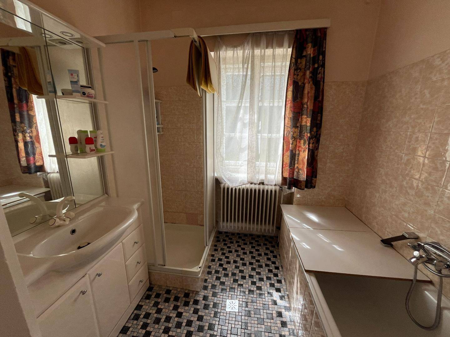 Badezimmer mit Dusche, Badewanne, Waschbecken und Fenster, im Stil der 80er Jahre.