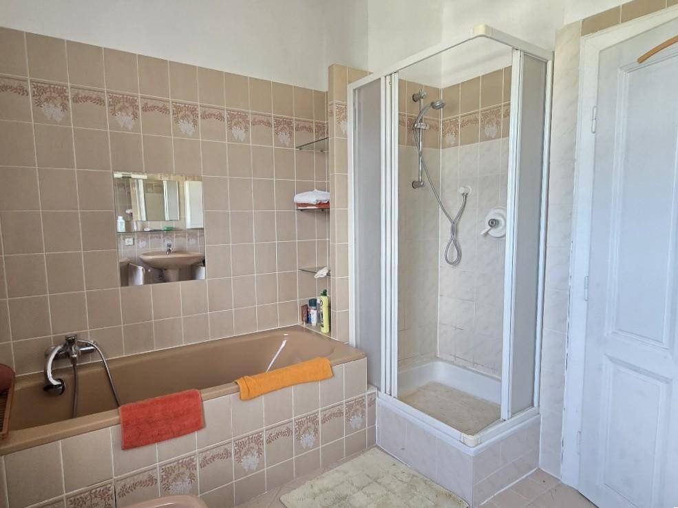 Badezimmer mit Badewanne, Duschkabine und beigen Fliesen.