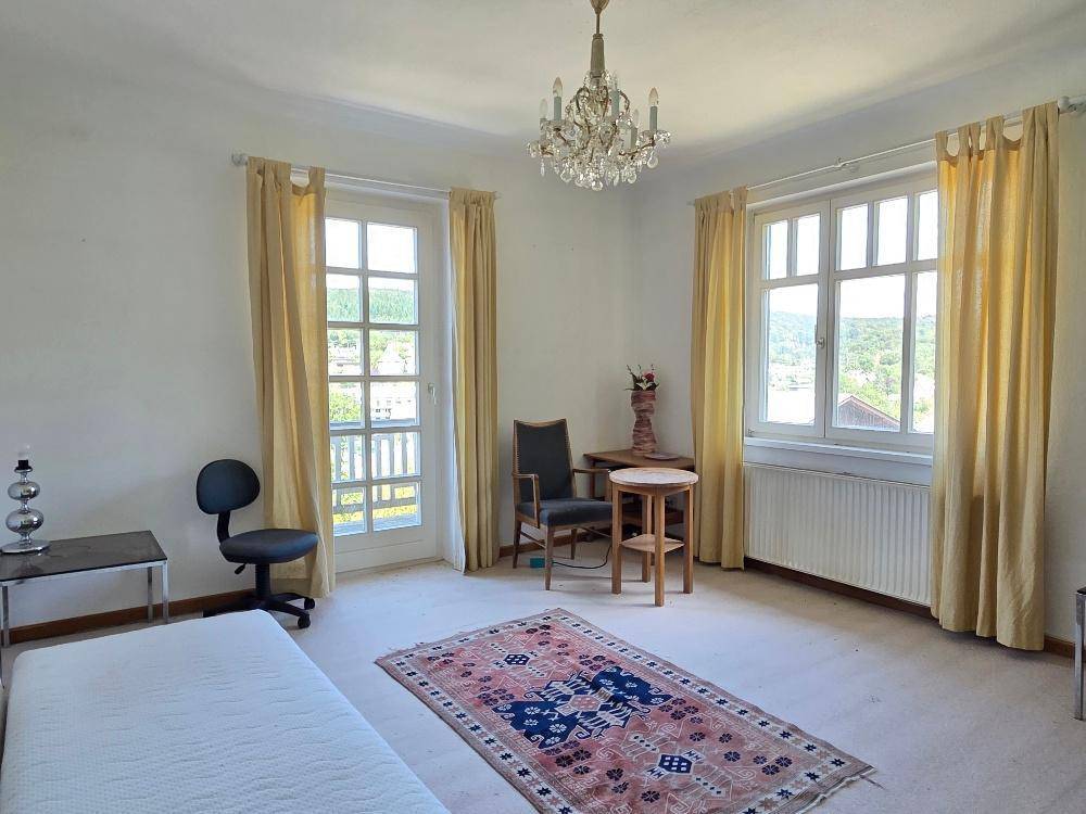 Helles Schlafzimmer mit Teppichboden, Kronleuchter und Zugang zum Balkon.