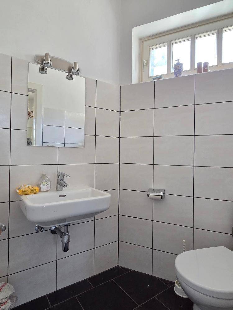 Kleines Gäste-WC mit weißen Fliesen, Fenster und dunklem Boden.