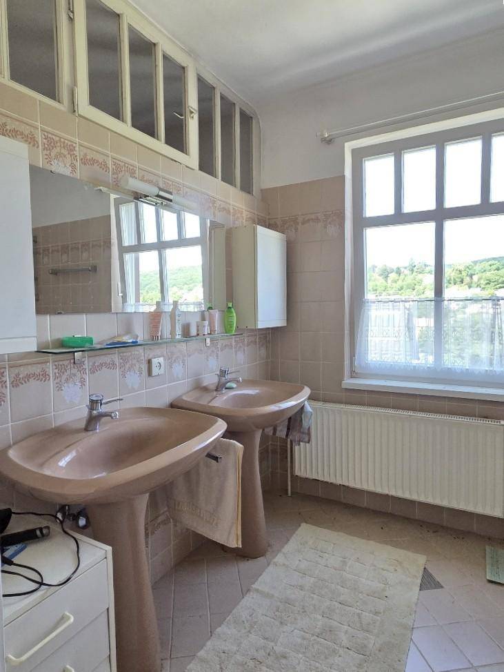 Geräumiges Badezimmer mit Doppelwaschbecken, beigen Fliesen und Fenster.