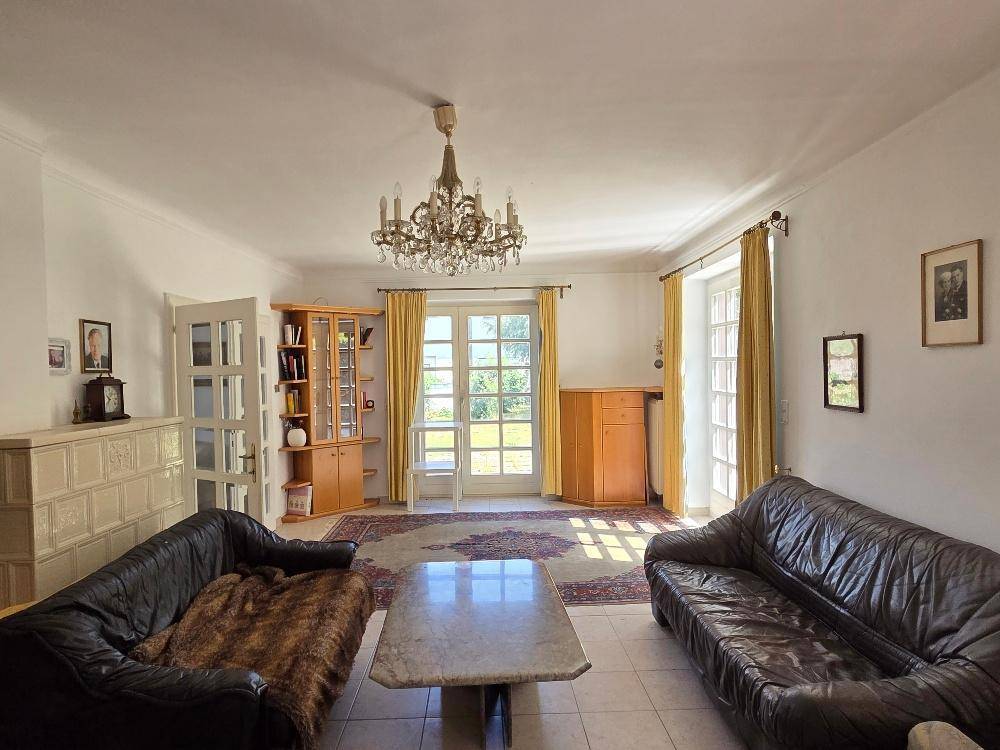 Helles Wohnzimmer mit traditionellem Kachelofen, Ledersofas und Zugang zum Garten.