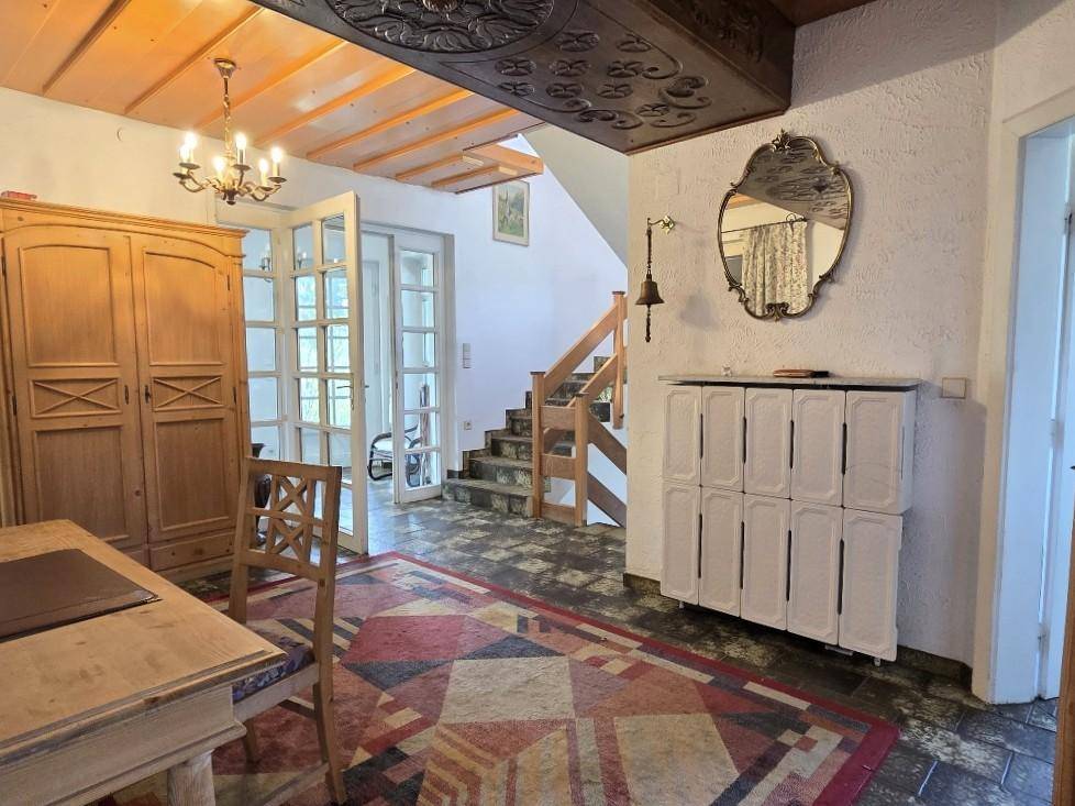 Eingangsbereich mit Holztreppe, Fliesenboden und geschnitzter Holzdecke.