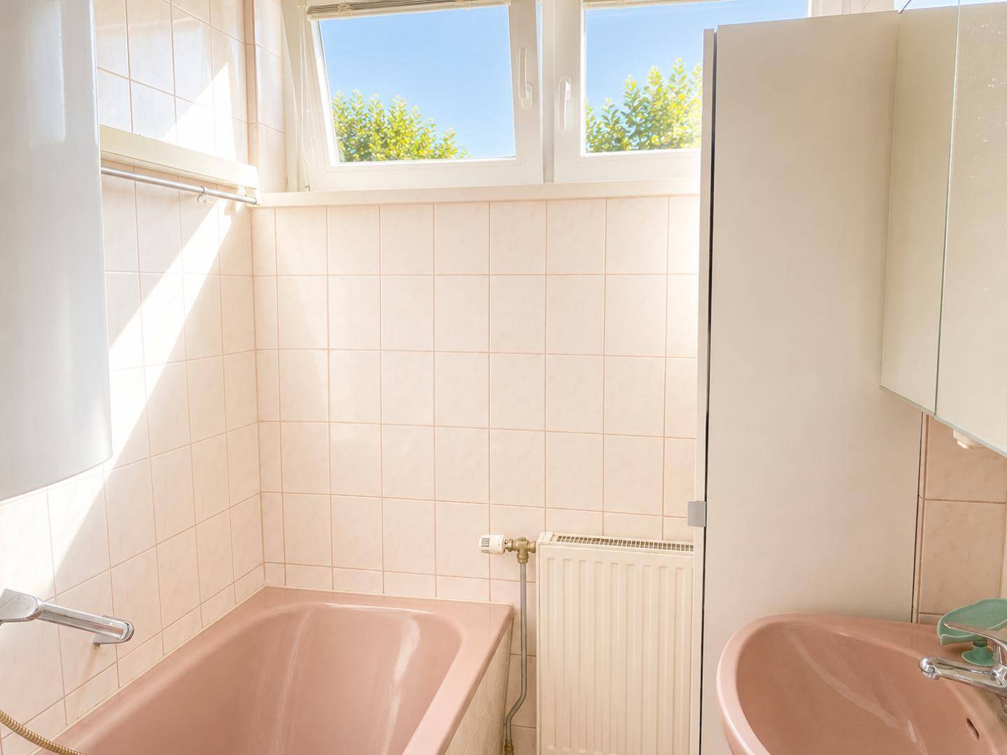 Helles Badezimmer mit rosa Sanitärobjekten, weißen Fliesen und Fenster.