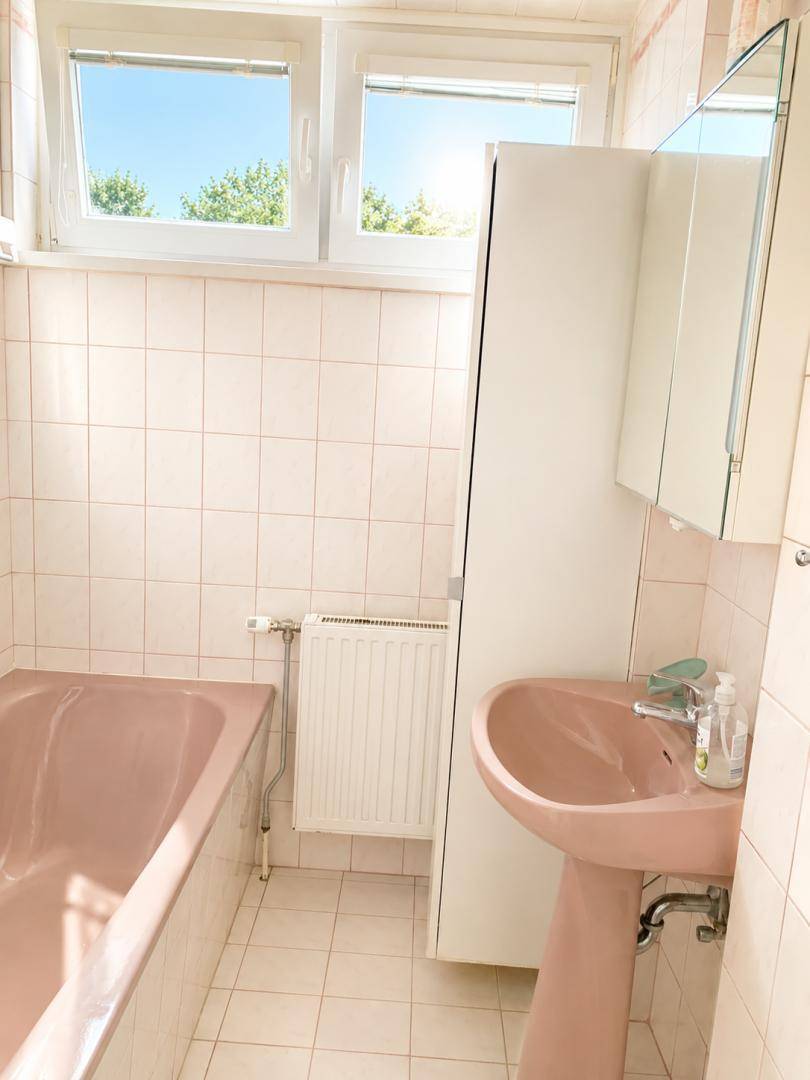 Badezimmer mit rosa Badewanne, passendem Waschbecken und hellen Fliesen.