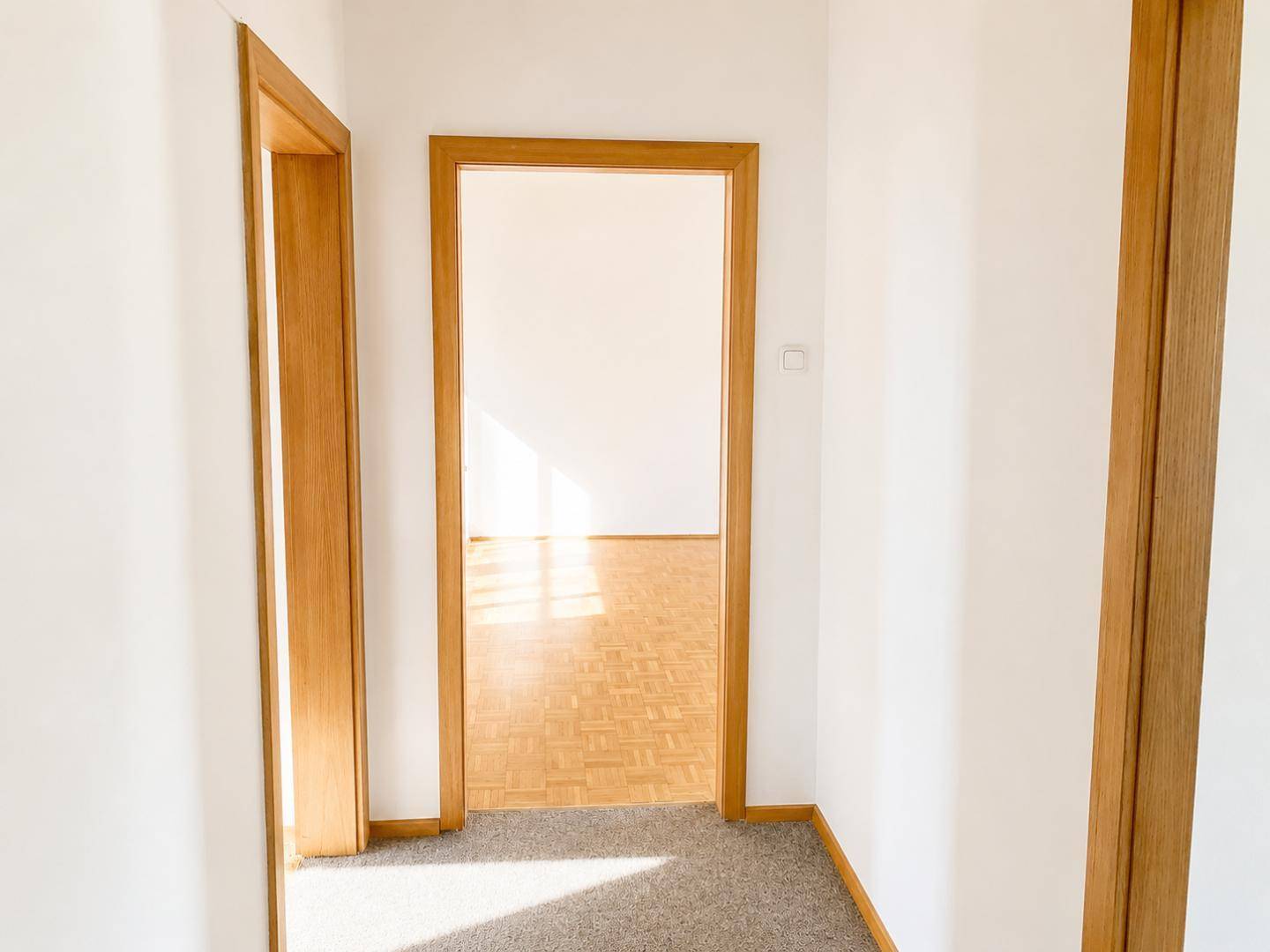 Heller Flur mit Teppichboden und Holztürrahmen, der in ein weiteres Zimmer führt.
