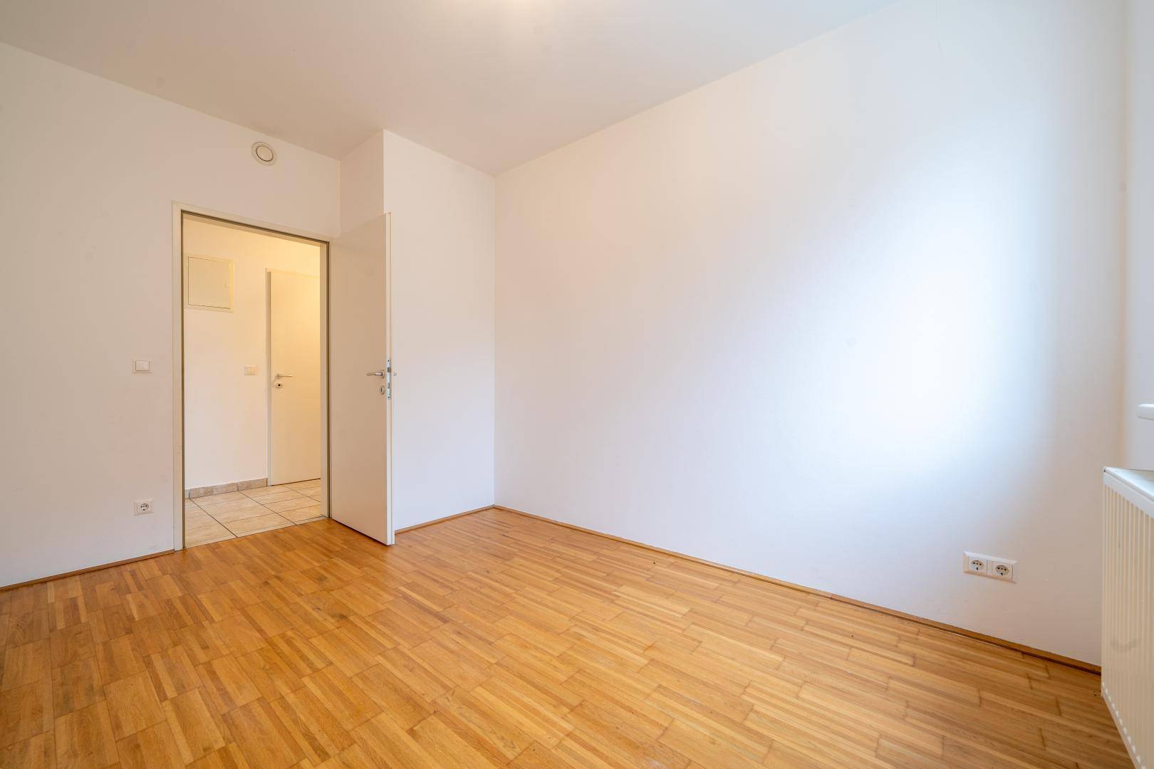 Ruhiges Schlafzimmer mit hellem Parkettboden und Zugang zu einem gefliesten Bereich.