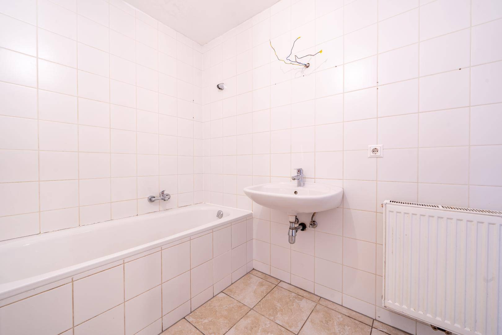 Funktionales Badezimmer mit Badewanne, Waschbecken und weißen Fliesen an Wänden und Boden.