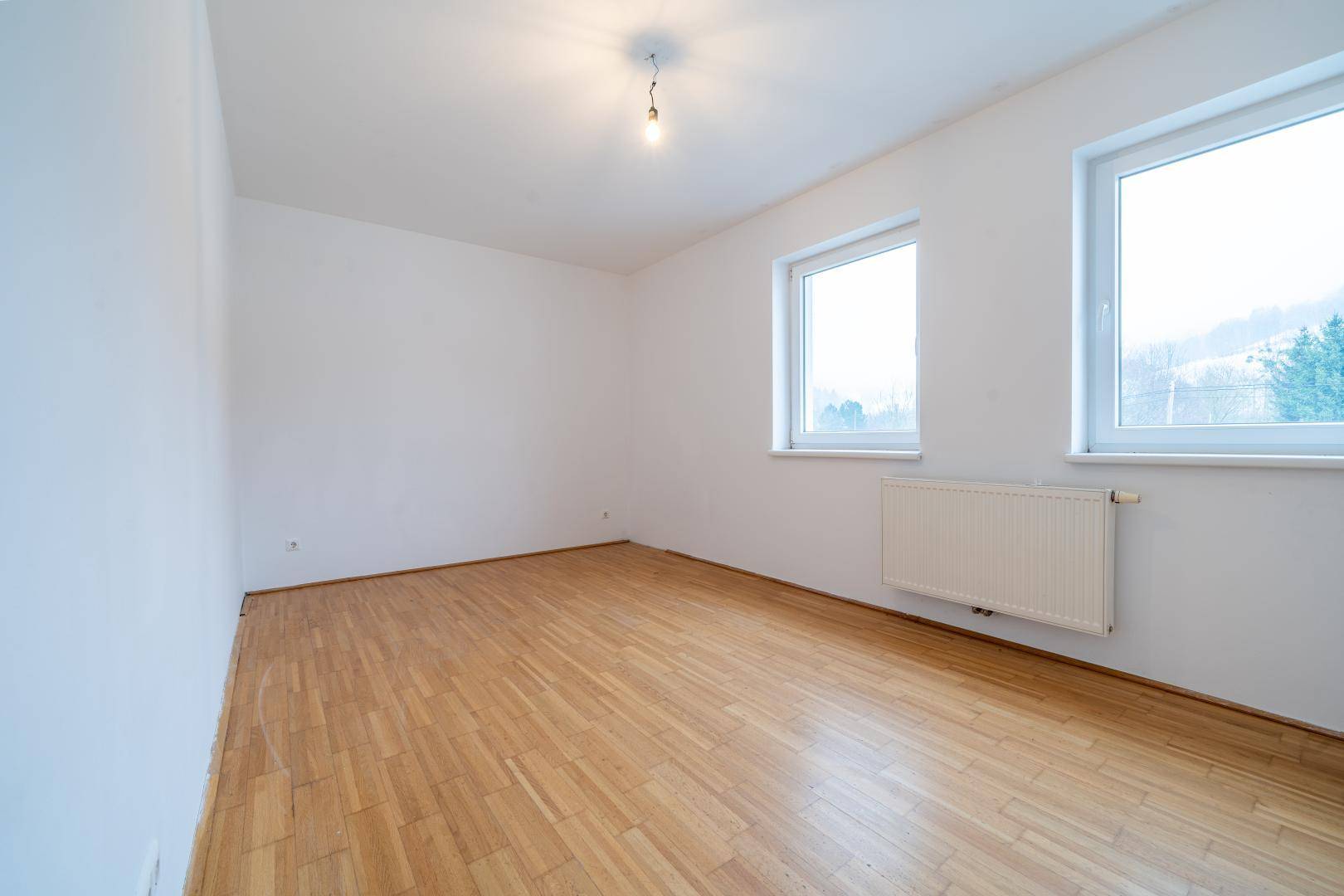 Helles Zimmer mit zwei Fenstern, Parkettboden und einem angenehmen Blick ins Grüne.