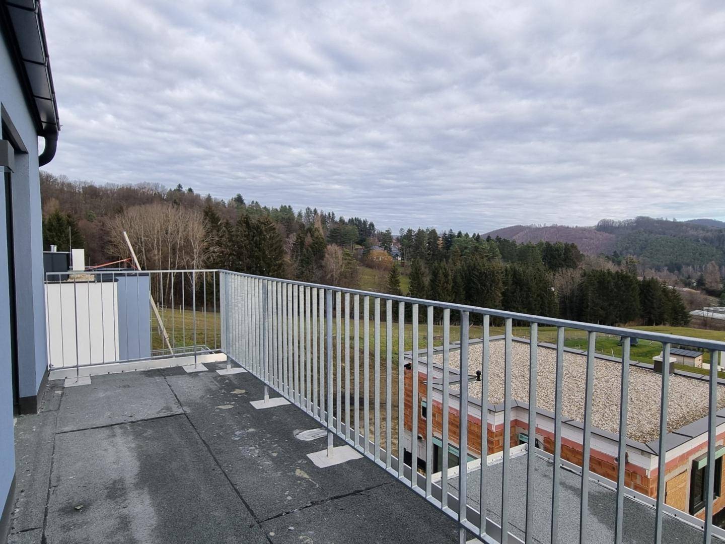 Balkon mit Metallgeländer und weitem Blick über die hügelige, bewaldete Landschaft.