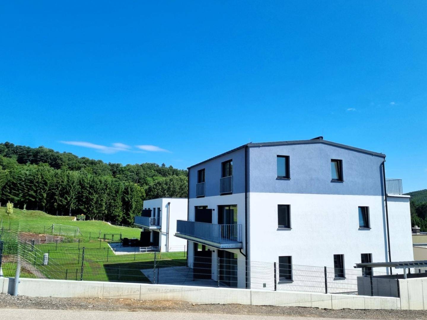 Modernes Mehrfamilienhaus mit blauer und weißer Fassade, umgeben von Grünflächen und Bäumen.